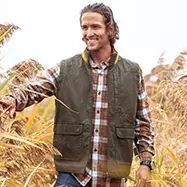 Man standing in field wearing vest.