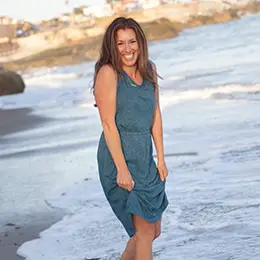 Woman walking in water on beach in dress.
